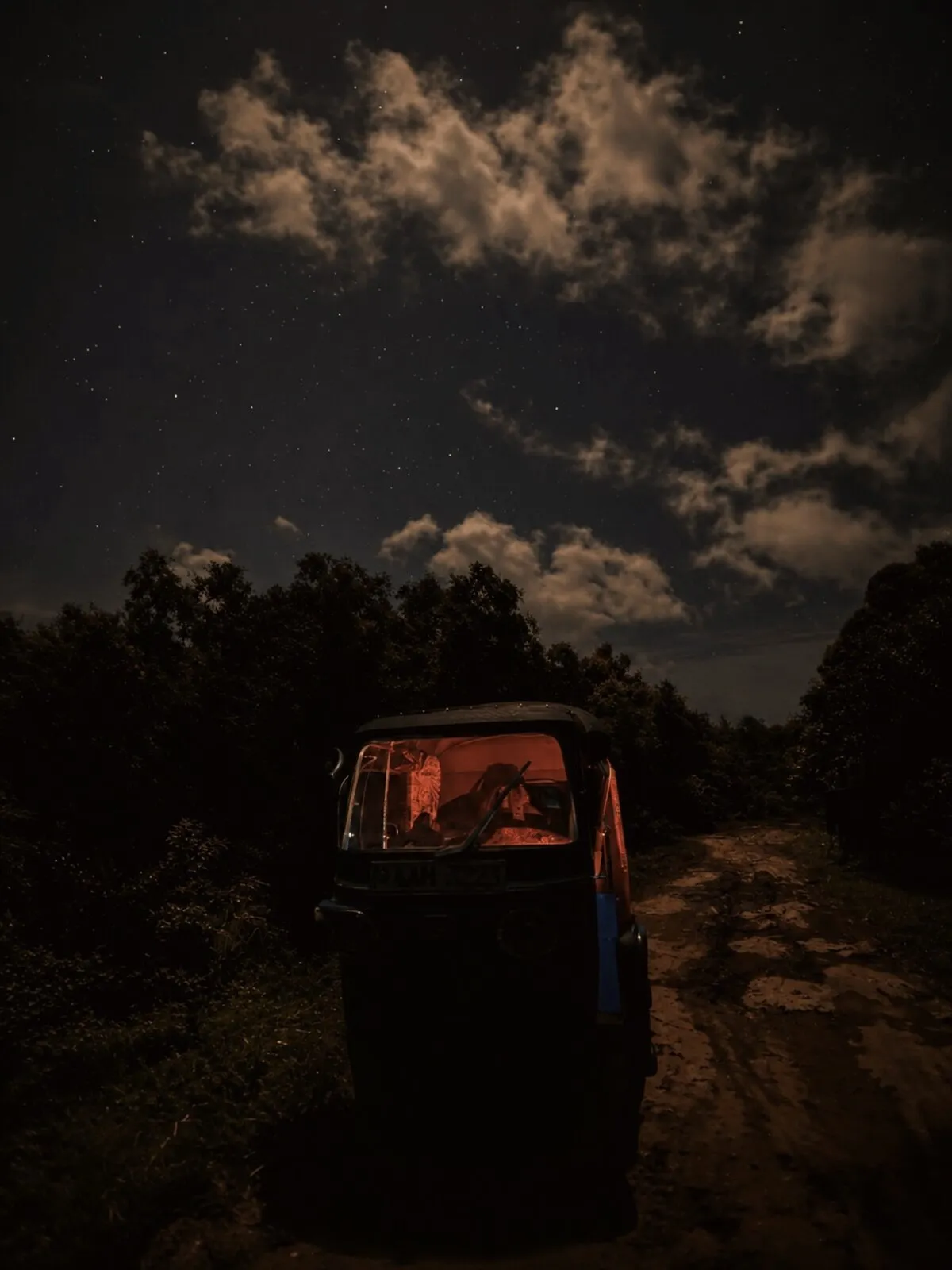 Tuk-tuk on a dark night road with taillights trailing behind